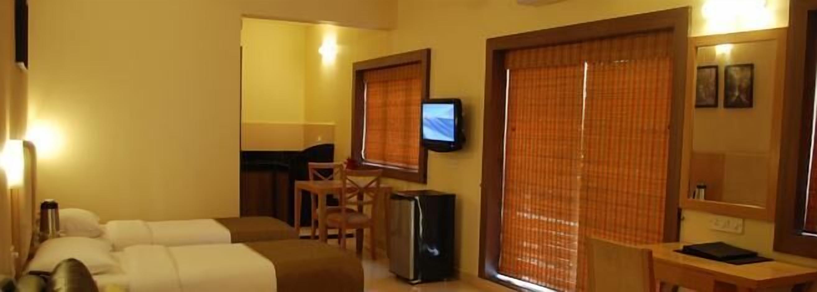 Una habitación de hotel con dos camas, un escritorio, un televisor y una ventana con persianas.