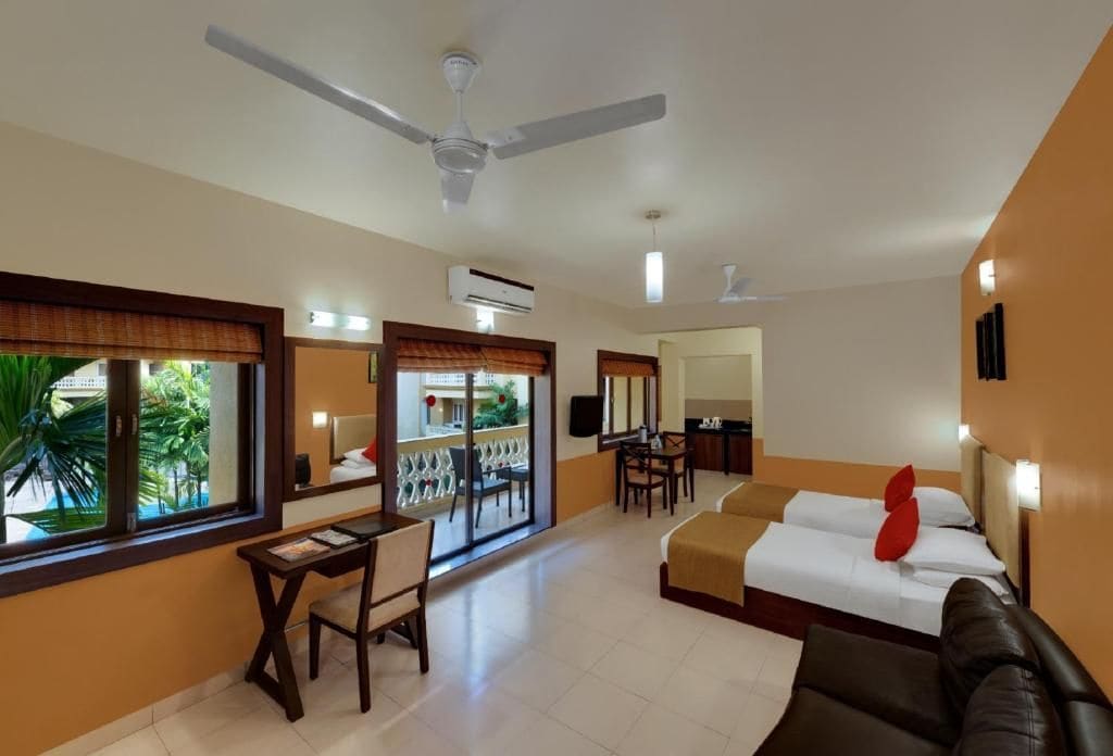 A hotel room with a bed, a desk, a chair, a balcony with a view, and a ceiling fan.