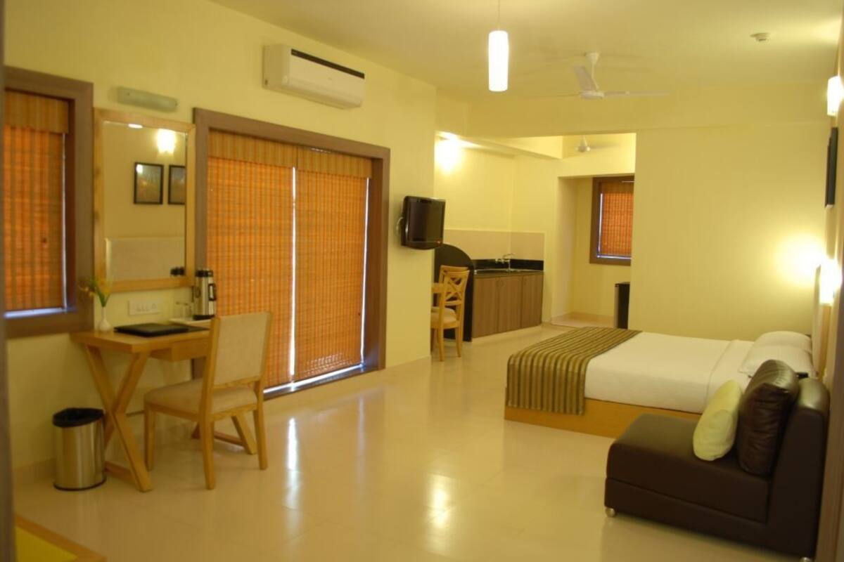 Habitación de hotel con cama, escritorio, silla, televisor y ventana con persianas.