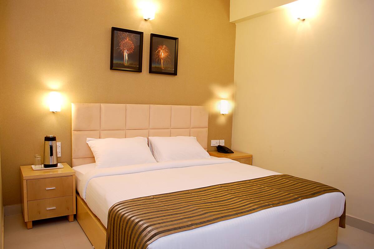 Habitación de hotel con cama, mesitas de noche y dos lámparas de pared.