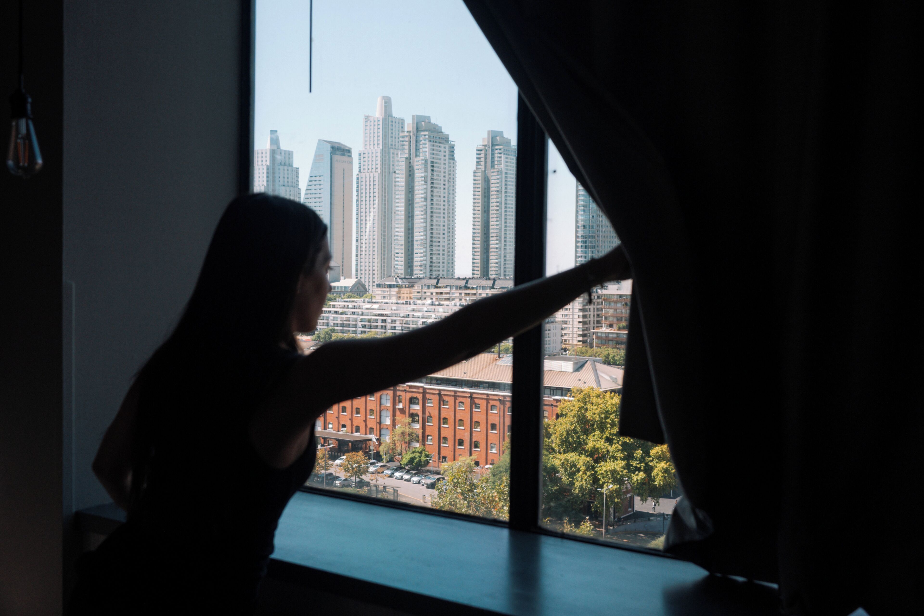 Una persona de pie junto a una ventana con vista a la ciudad.