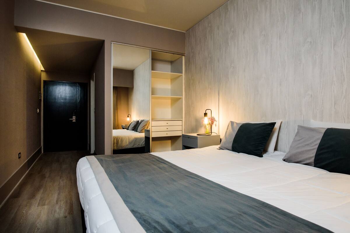 A modern hotel room with a large bed, a walk-in closet, and a bedside table with a lamp.