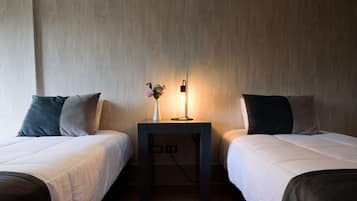 A hotel room with two single beds, a small table with a vase of flowers, and a wall-mounted light.