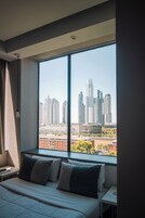 Habitación de hotel con un ventanal grande, una cama, una mesita de noche y vistas a un paisaje urbano.