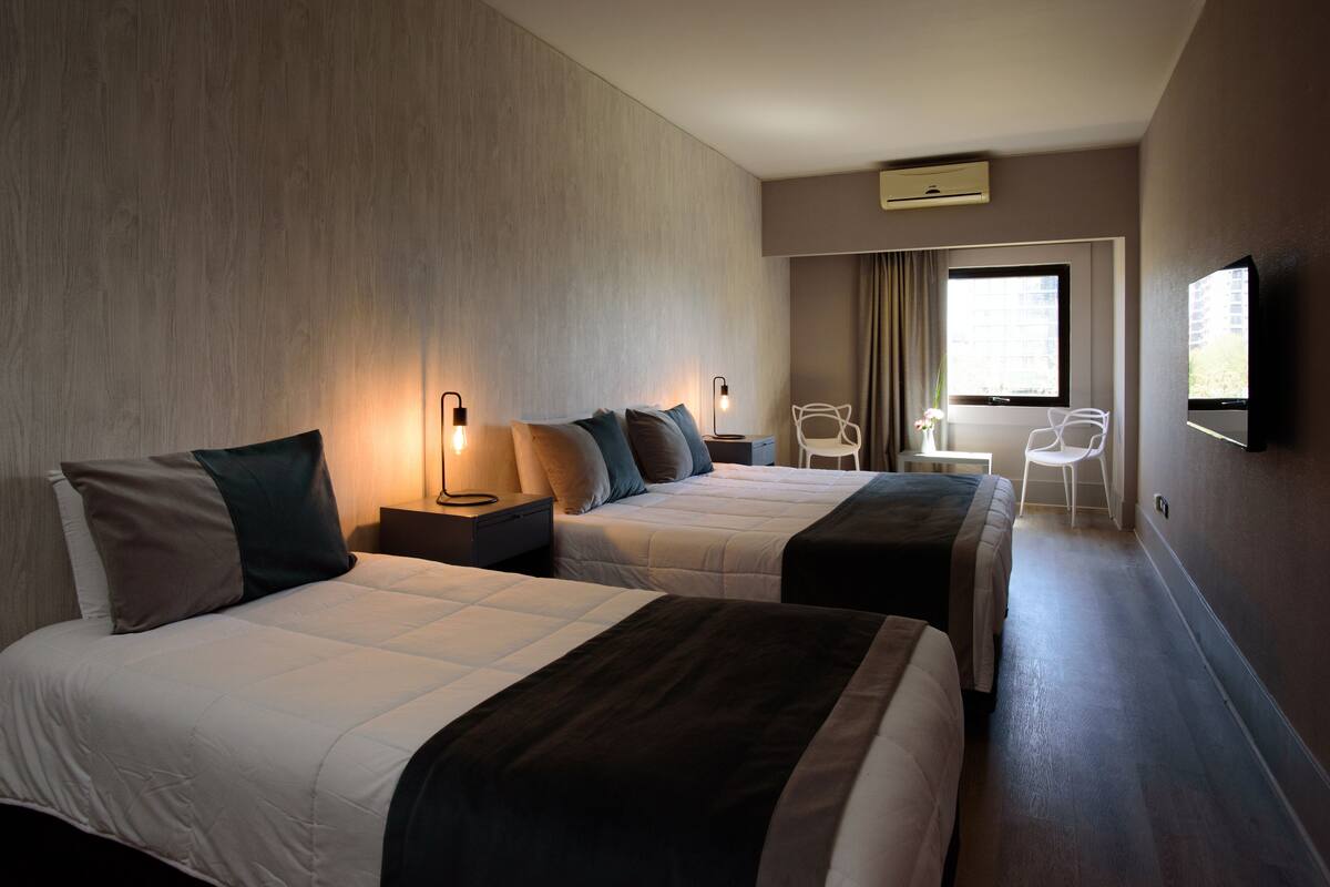 A hotel room with two beds, a desk, a chair, and a television.