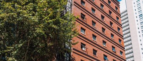 A multi-story building with a brick facade, a large tree in front, and a clear blue sky.
