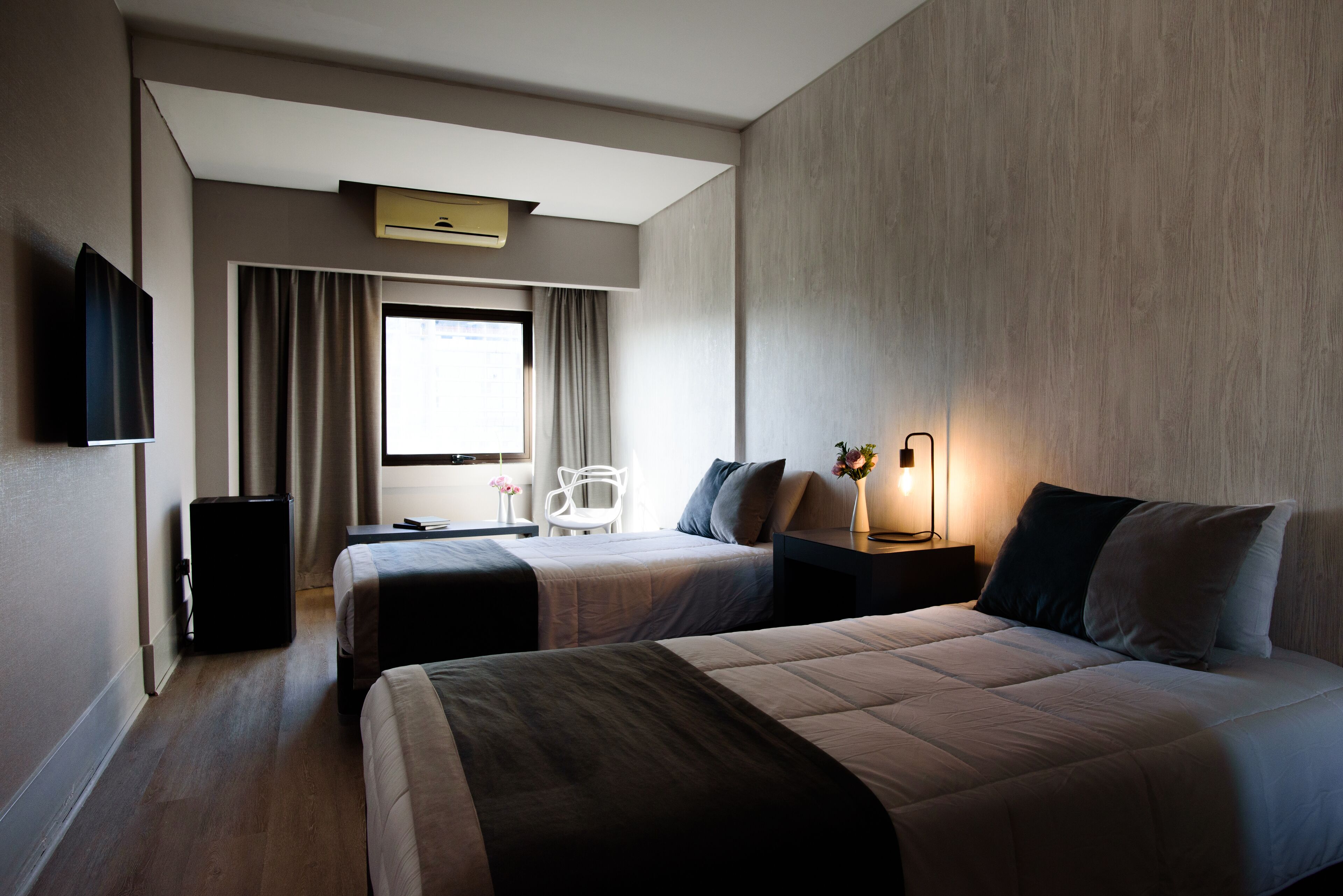 A hotel room with two beds, a desk, a chair, a TV, and a window with curtains.