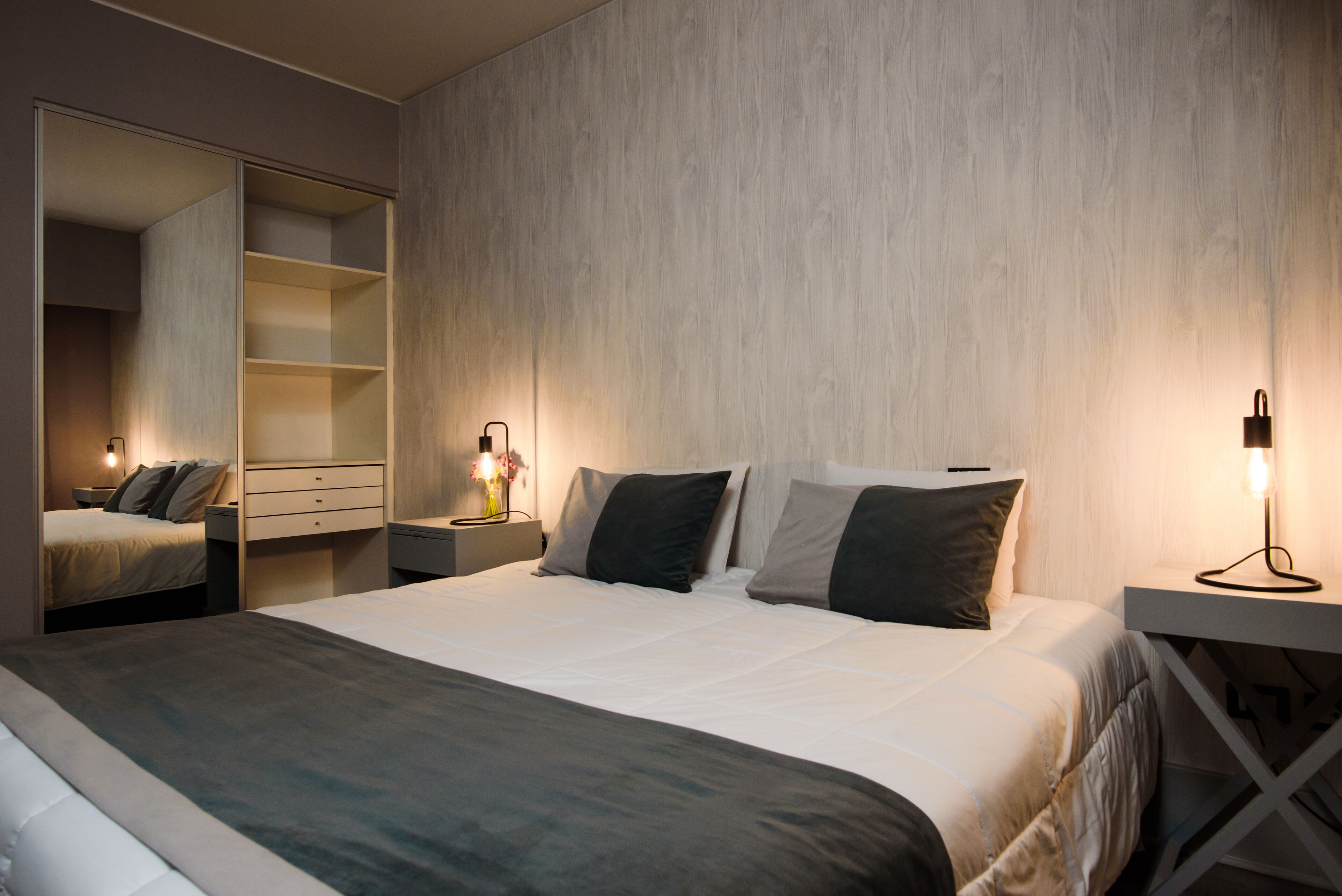Une chambre moderne avec un grand lit, une armoire avec un miroir, des tables de chevet avec des lampes et une palette de couleurs neutres.