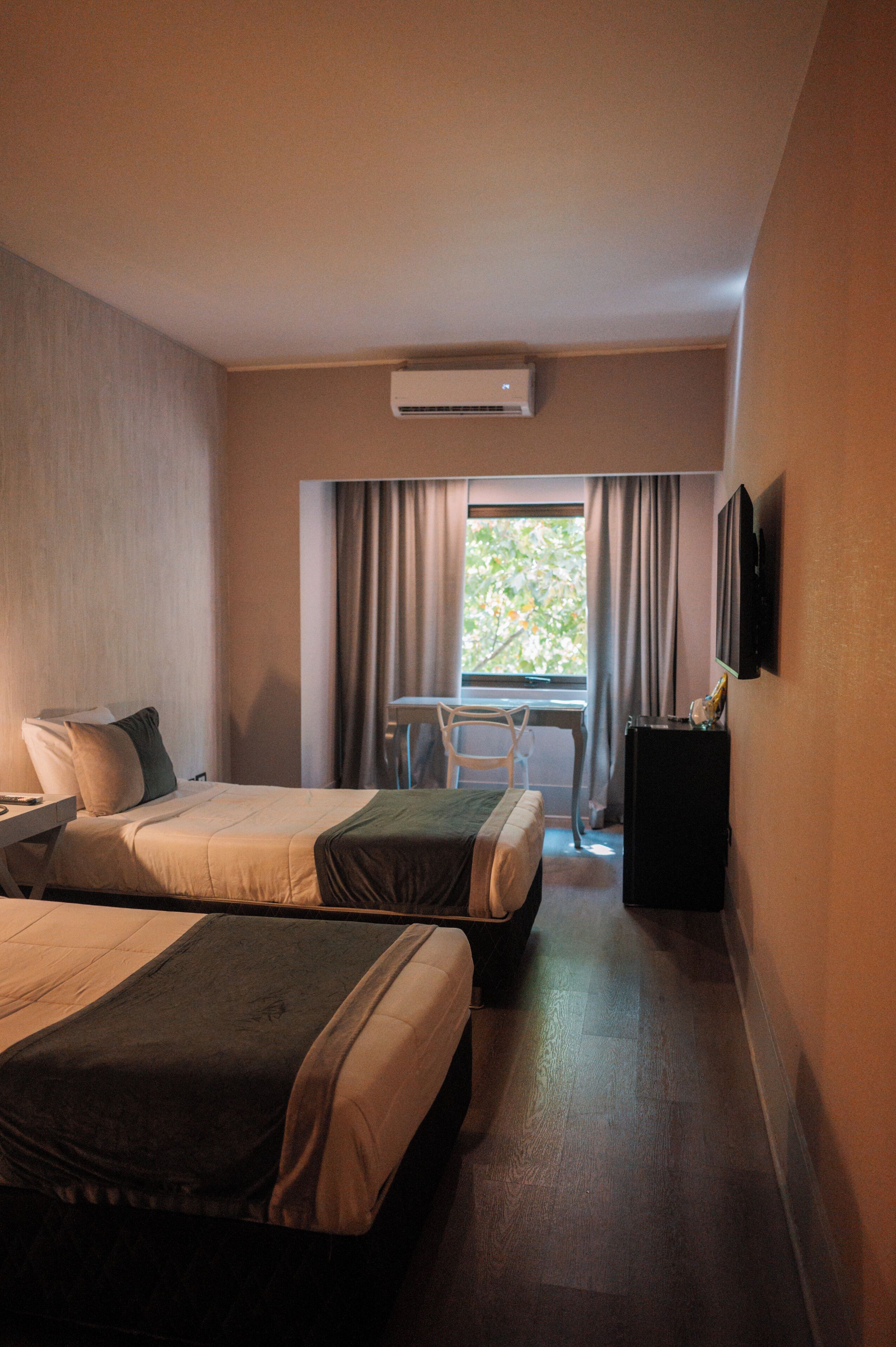 A hotel room with two beds, a desk, a chair, a TV, and a window with curtains.