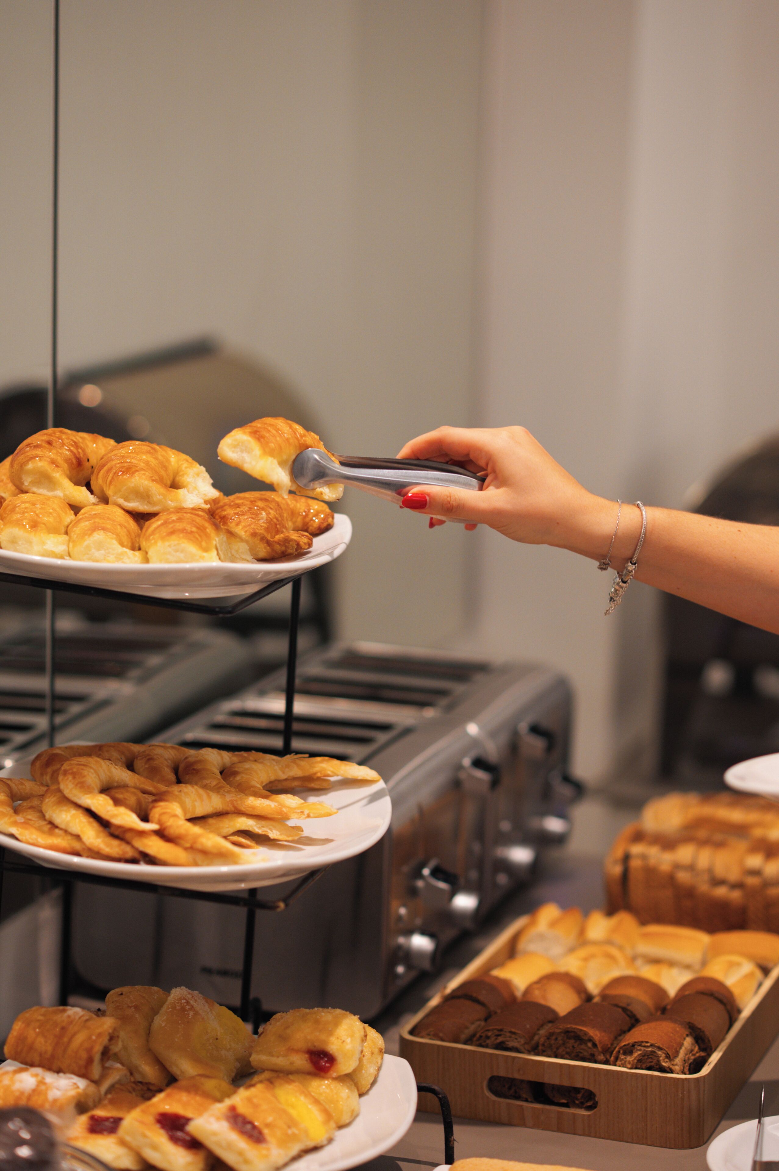 A buffet with various pastries and a hand using tongs to serve food.