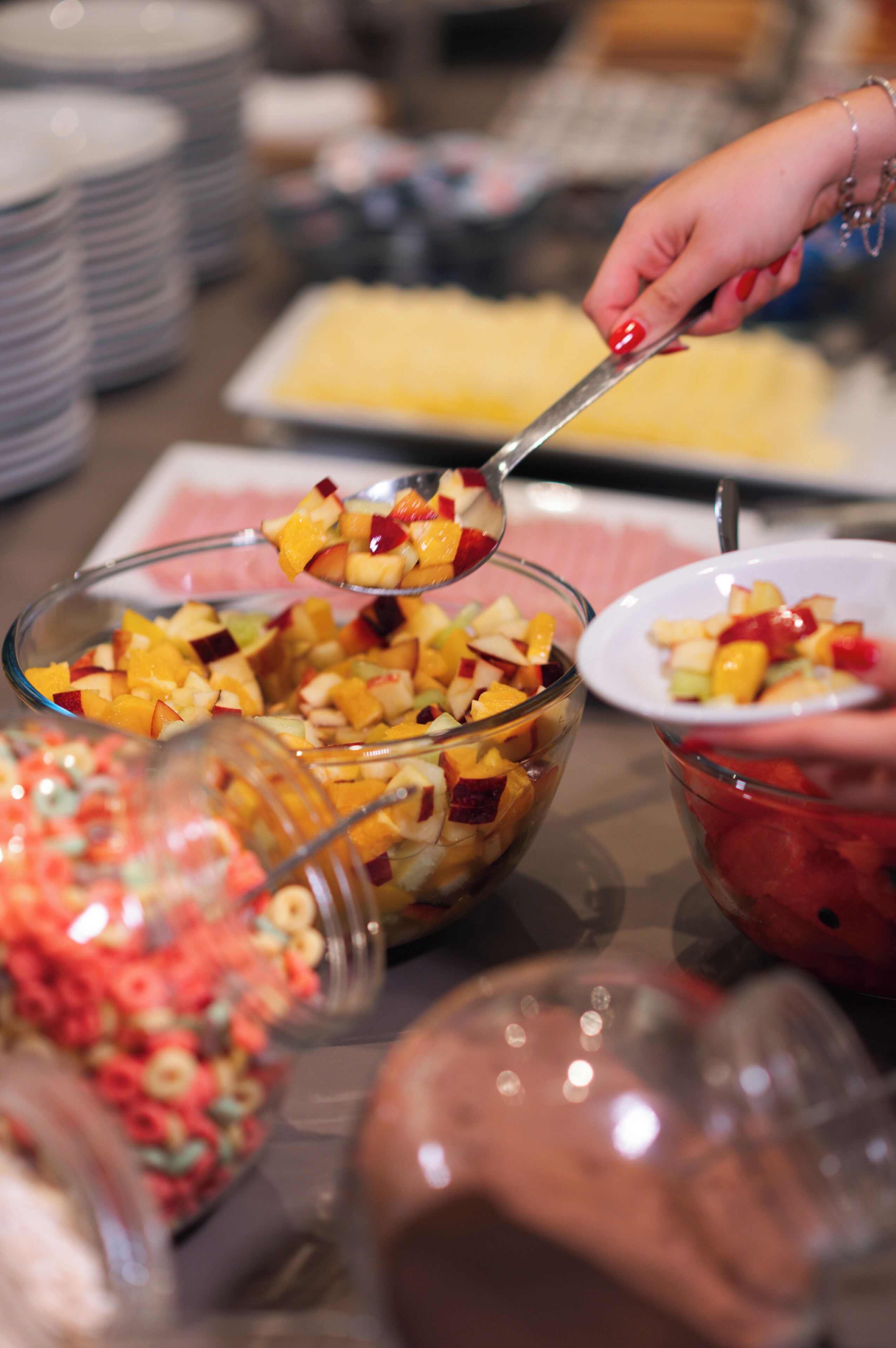 A buffet table with various food items and a person serving fruit.