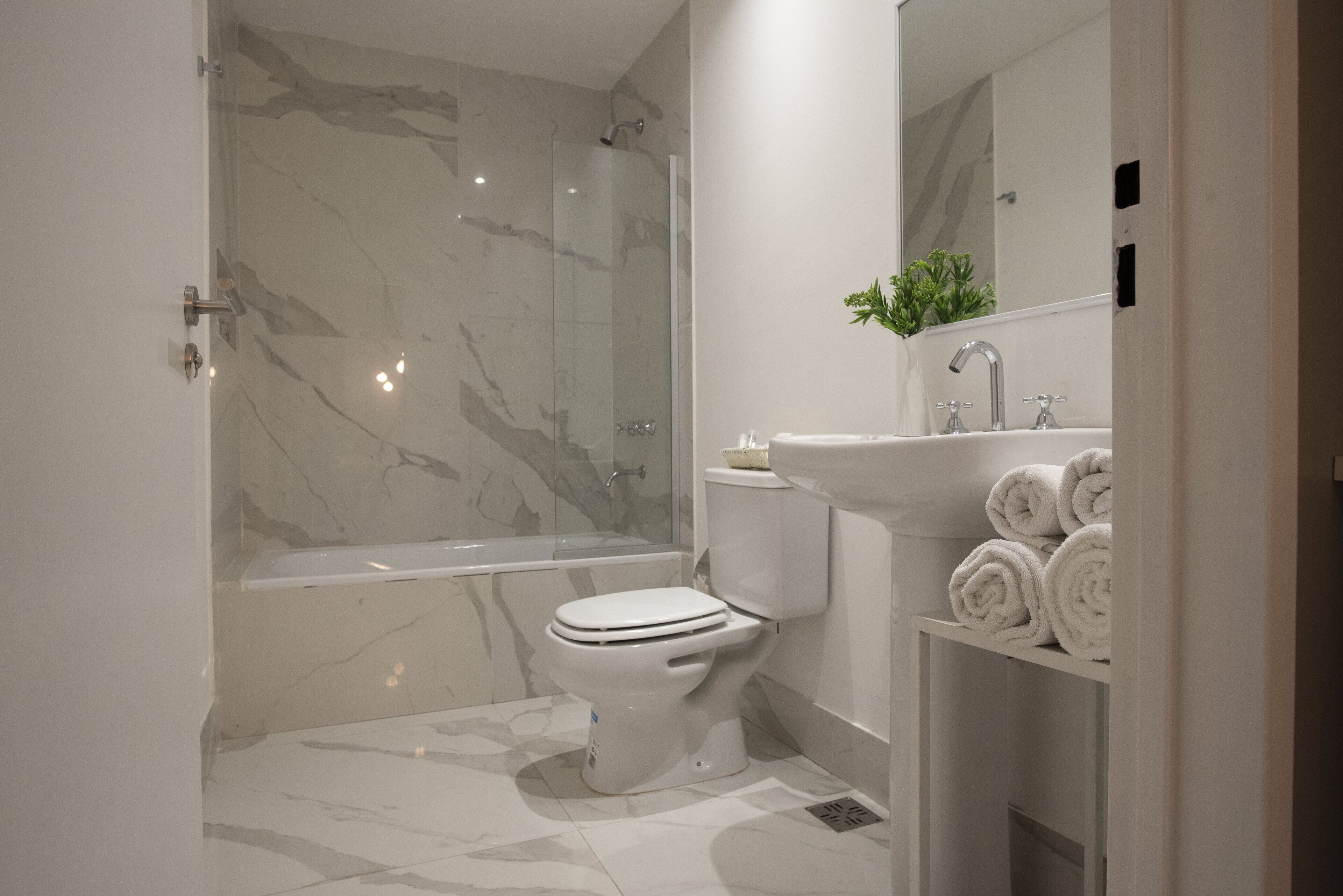 A modern bathroom with a glass-enclosed shower, a white toilet, and a sink with towels.