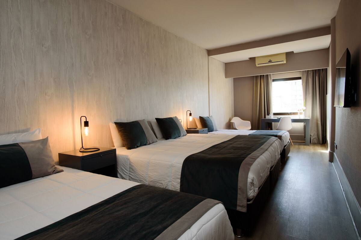 A hotel room with two beds, a desk, and a window with curtains.