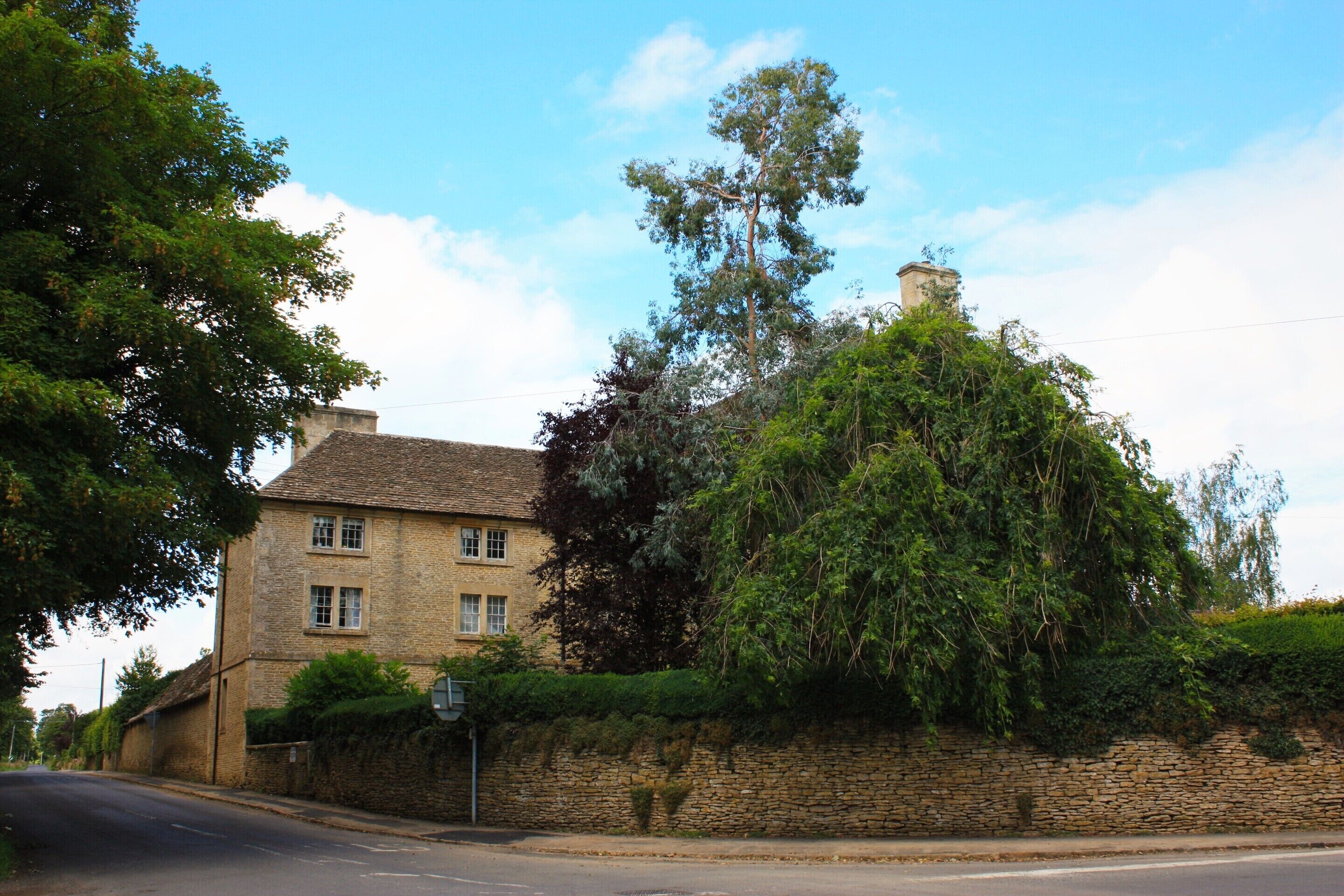 A traditional stone house with a prominent chimney, surrounded by lush greenery and a stone wall.