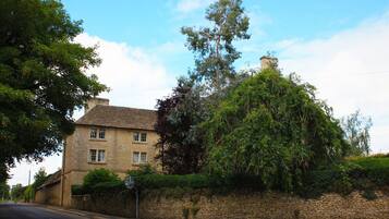 A traditional stone house with a prominent chimney, surrounded by lush greenery and a stone wall.