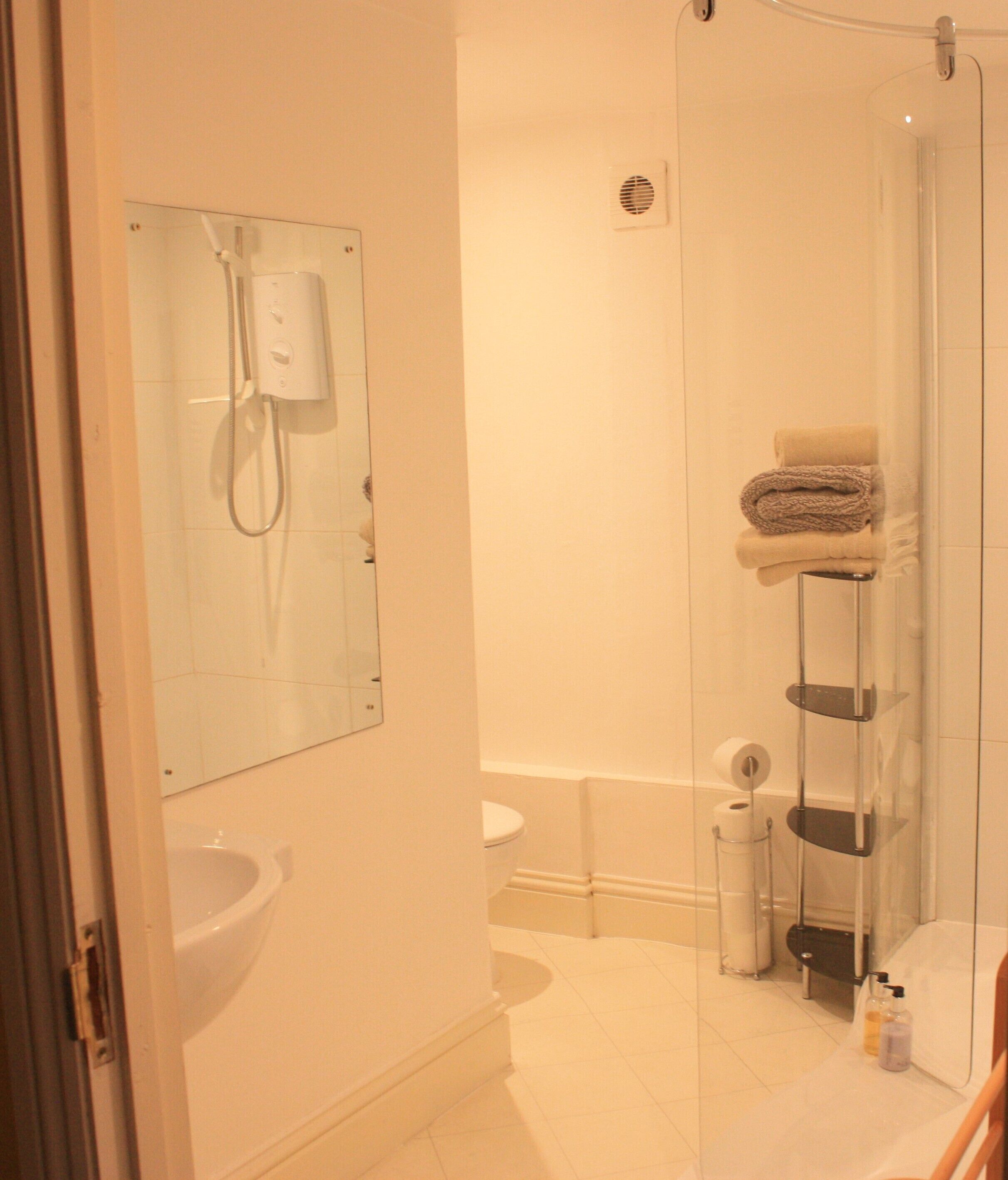 Un baño con cabina de ducha de vidrio, inodoro, lavabo y un perchero para toallas.