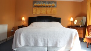 A hotel room with a large bed, two bedside tables with lamps, a dresser, a mirror, and a painting on the wall. - Manor Farm Bed & Breakfast (Chippenham)