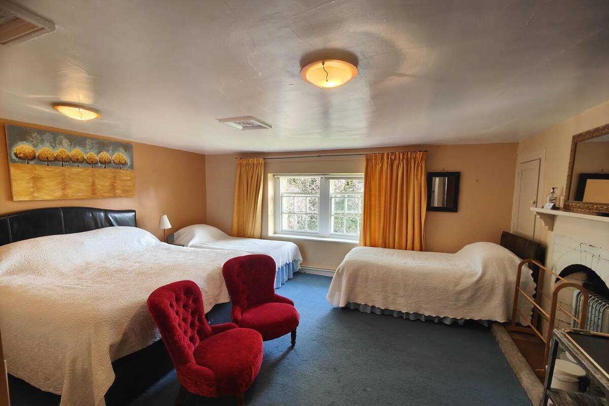 A hotel room with two beds, a red armchair, a window with curtains, a painting on the wall, and a fireplace.