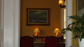 A hallway with a patterned floor, a dining area with two chairs and a table, and a lamp on the wall. - Manor Farm Bed & Breakfast (Chippenham)