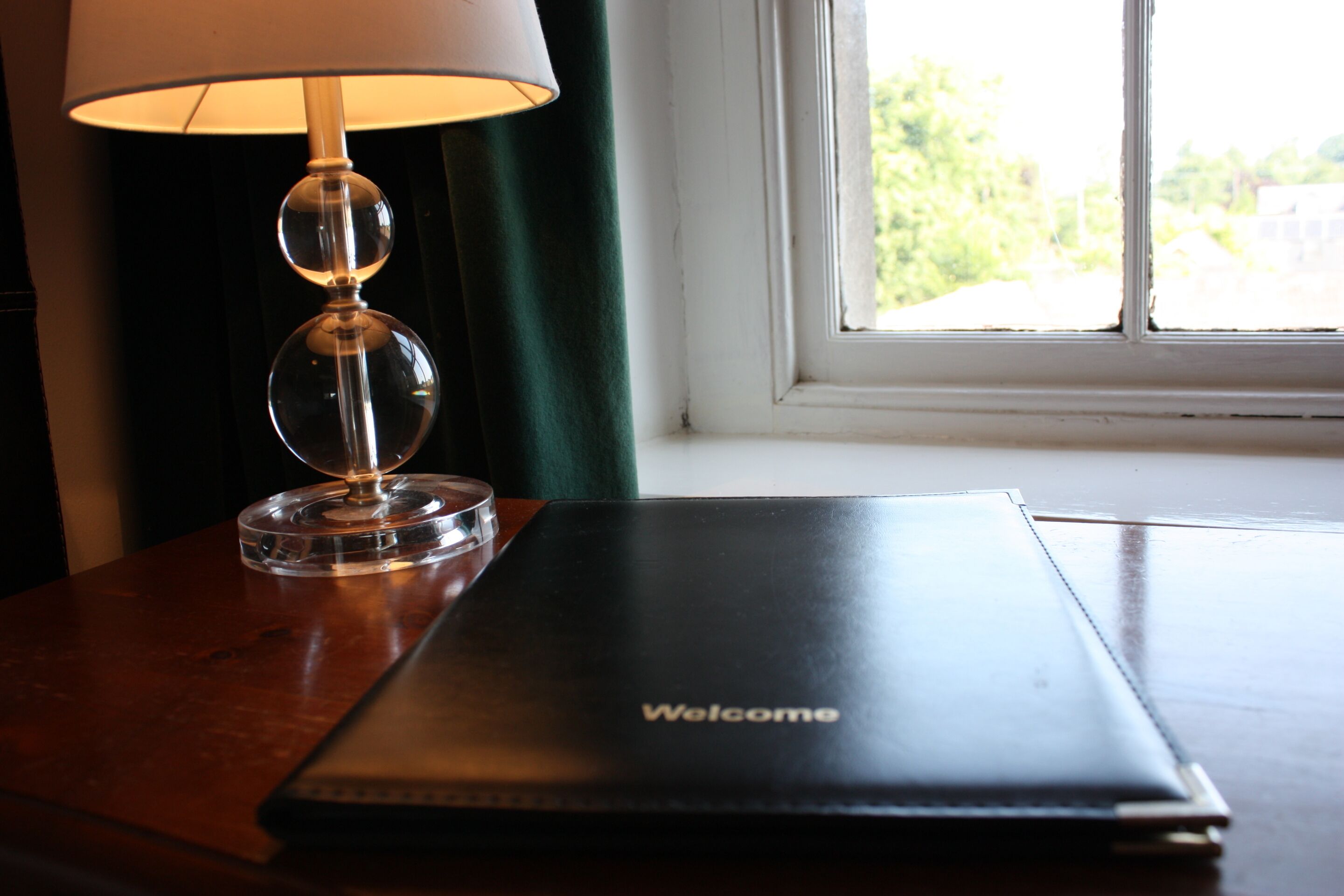 A welcome folder on a wooden table next to a lamp with a clear shade.