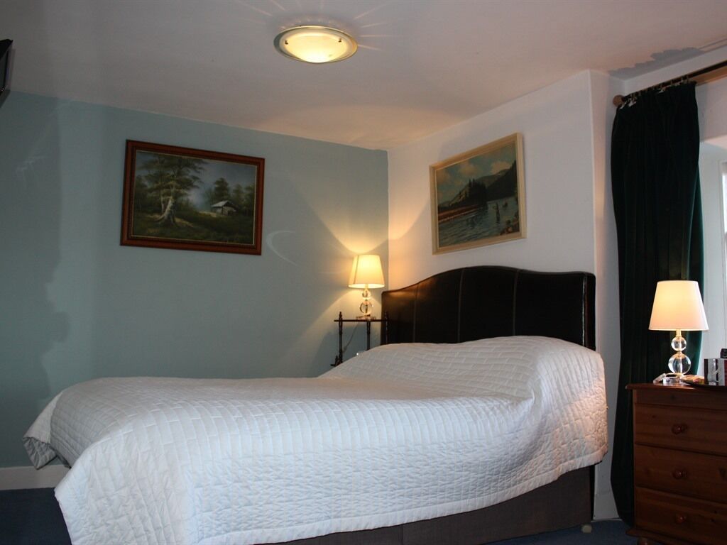 A bedroom with a bed, two wall-mounted lamps, and two paintings.