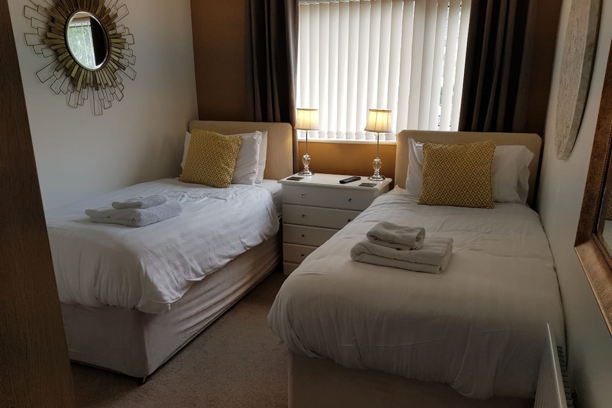Habitación de hotel con dos camas, una mesita de noche, un espejo y una ventana con persianas.