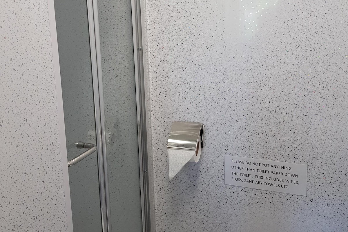 Un baño con ducha, dispensador de papel higiénico y un letrero que indica no arrojar nada más que papel higiénico al inodoro.