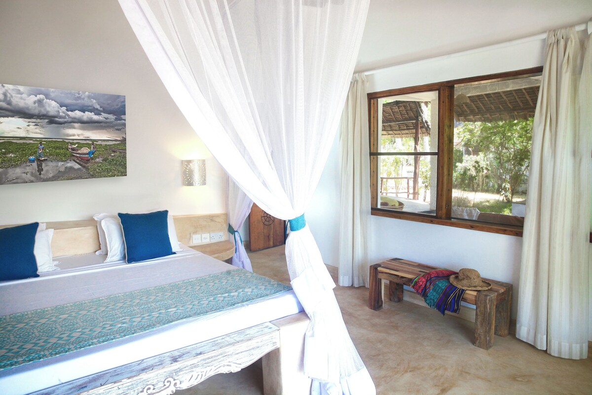 Un dormitorio con cama, un banco, una ventana y un cuadro en la pared.