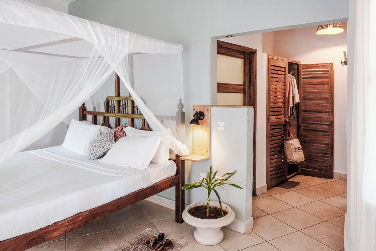 Un dormitorio con cama, mesita de noche, planta en maceta, armario y espejo.