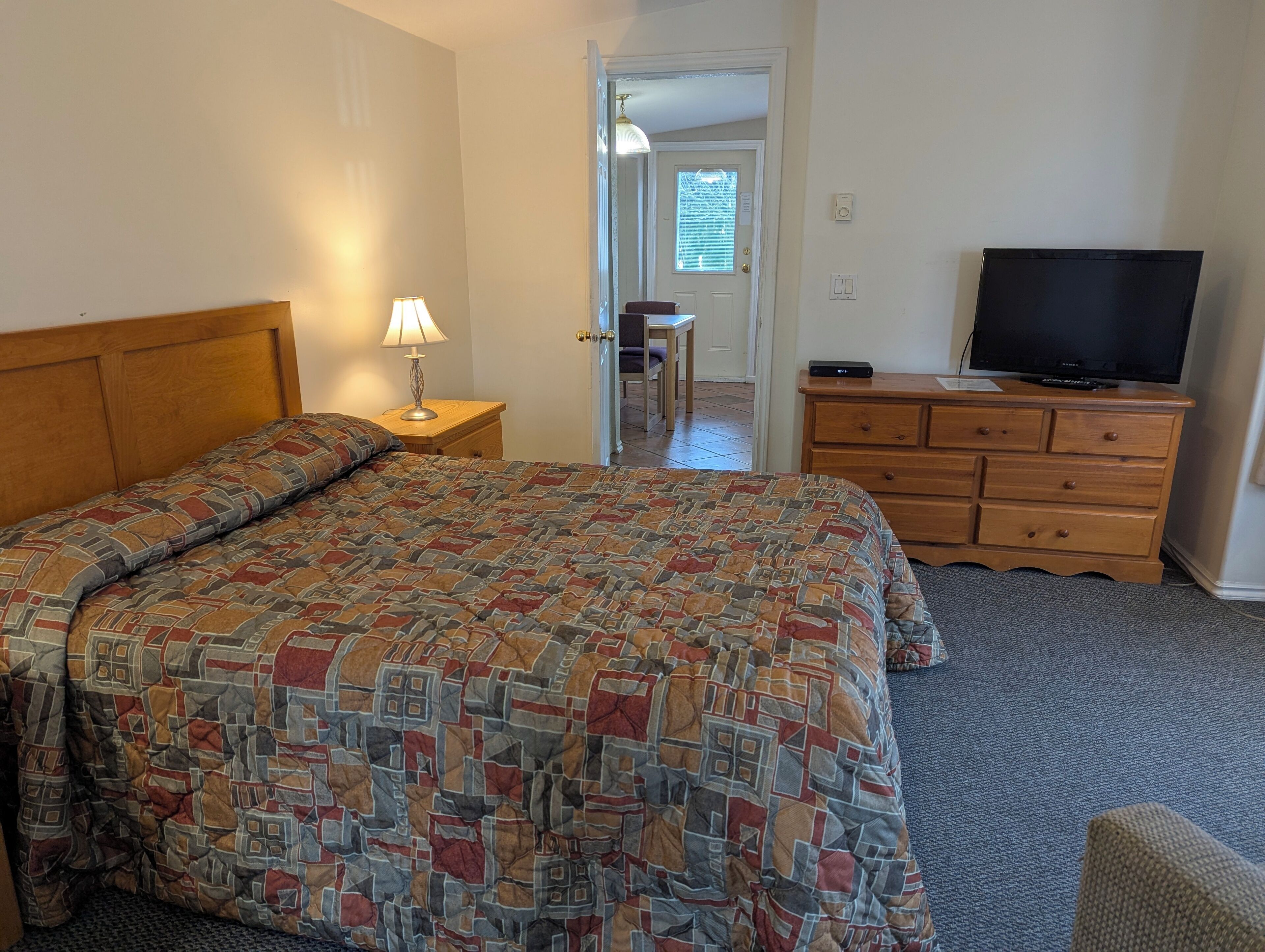 A bedroom with a bed, a dresser, a television, and a lamp.