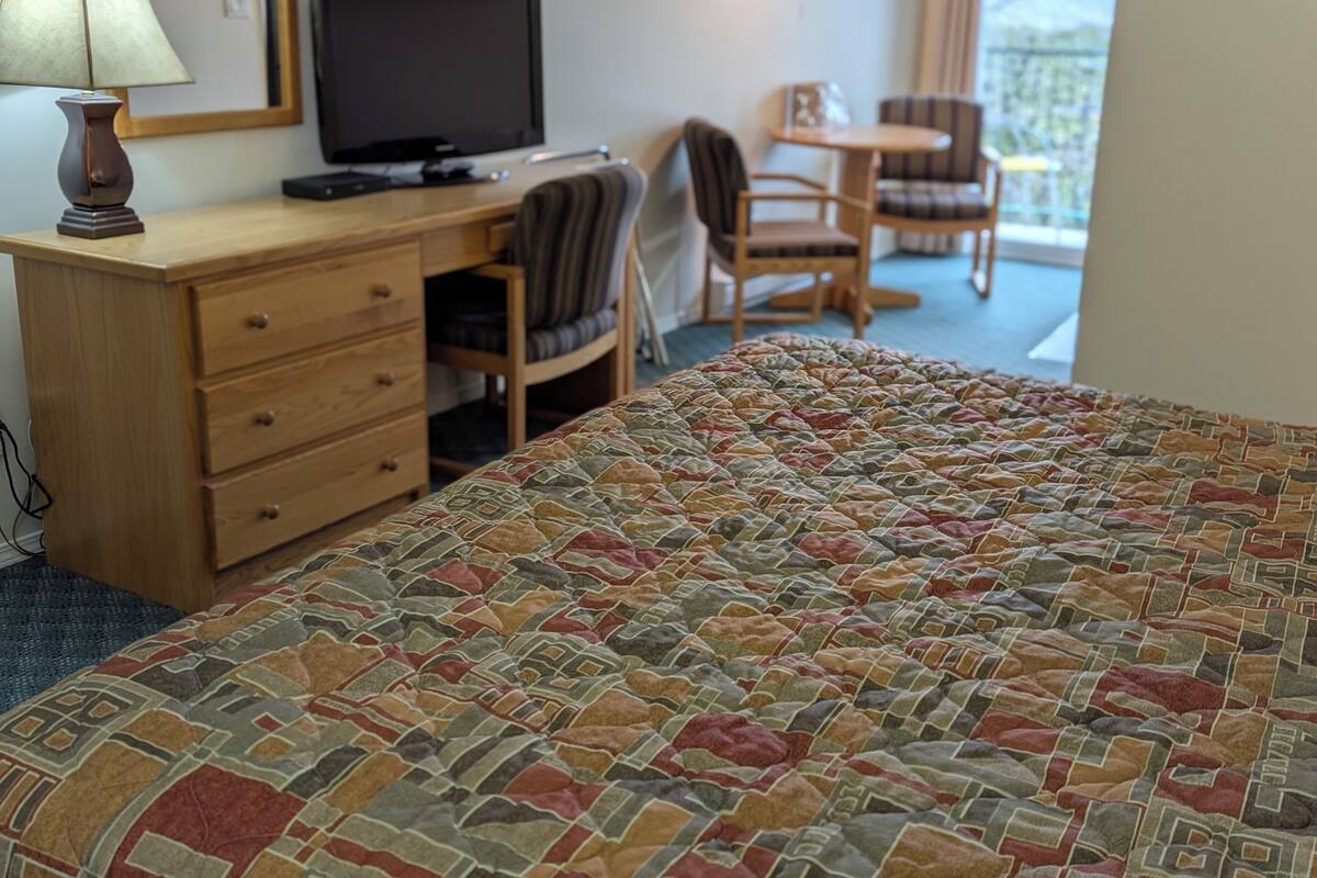 A hotel room with a bed, a desk with a computer, a chair, and a view of the outdoors.