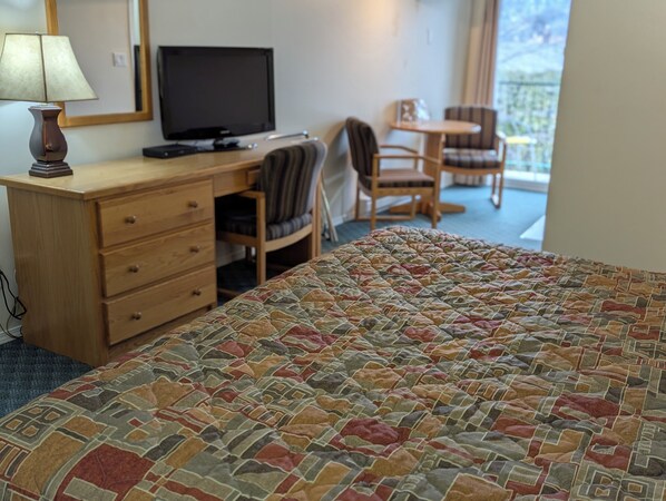 A hotel room with a bed, a desk with a computer, a chair, and a view of the outdoors. - Summerland Motel (Summerland)