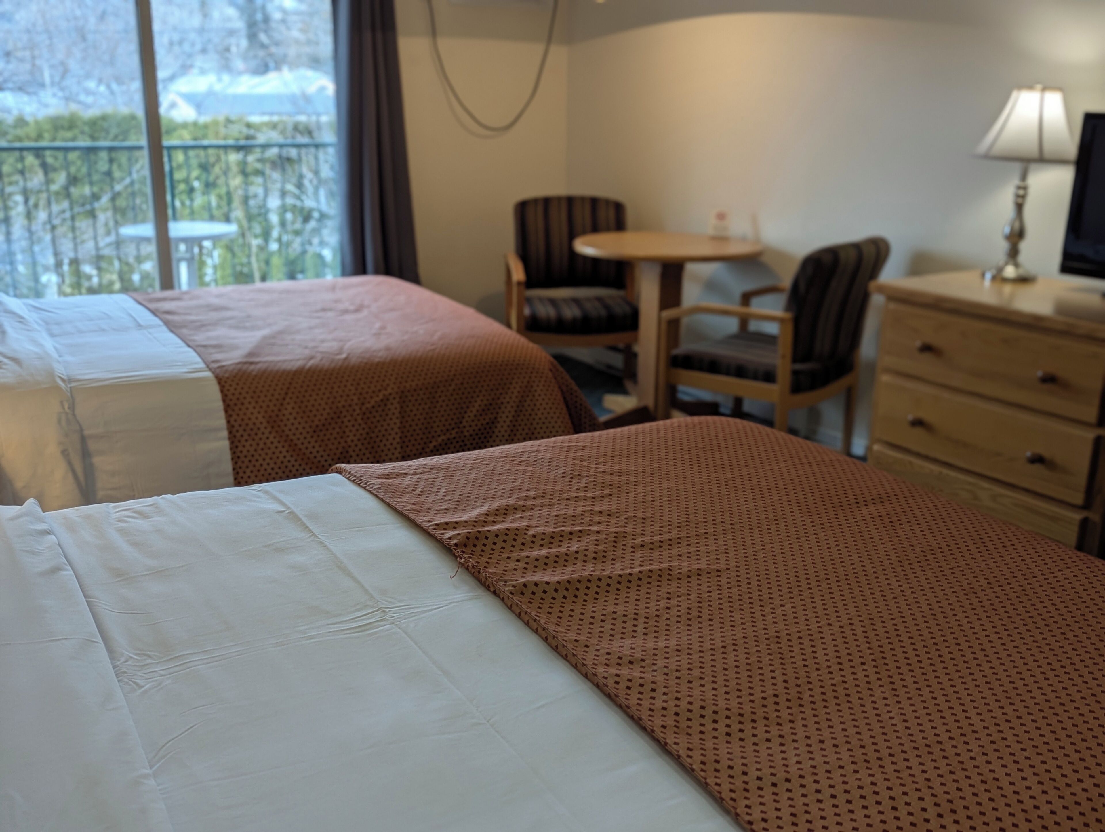 Et hotelværelse med to senge, et lille bord, en stol og en kommode.