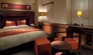 Een hotelkamer met een groot bed, een bureau, een stoel en een klein tafeltje.
