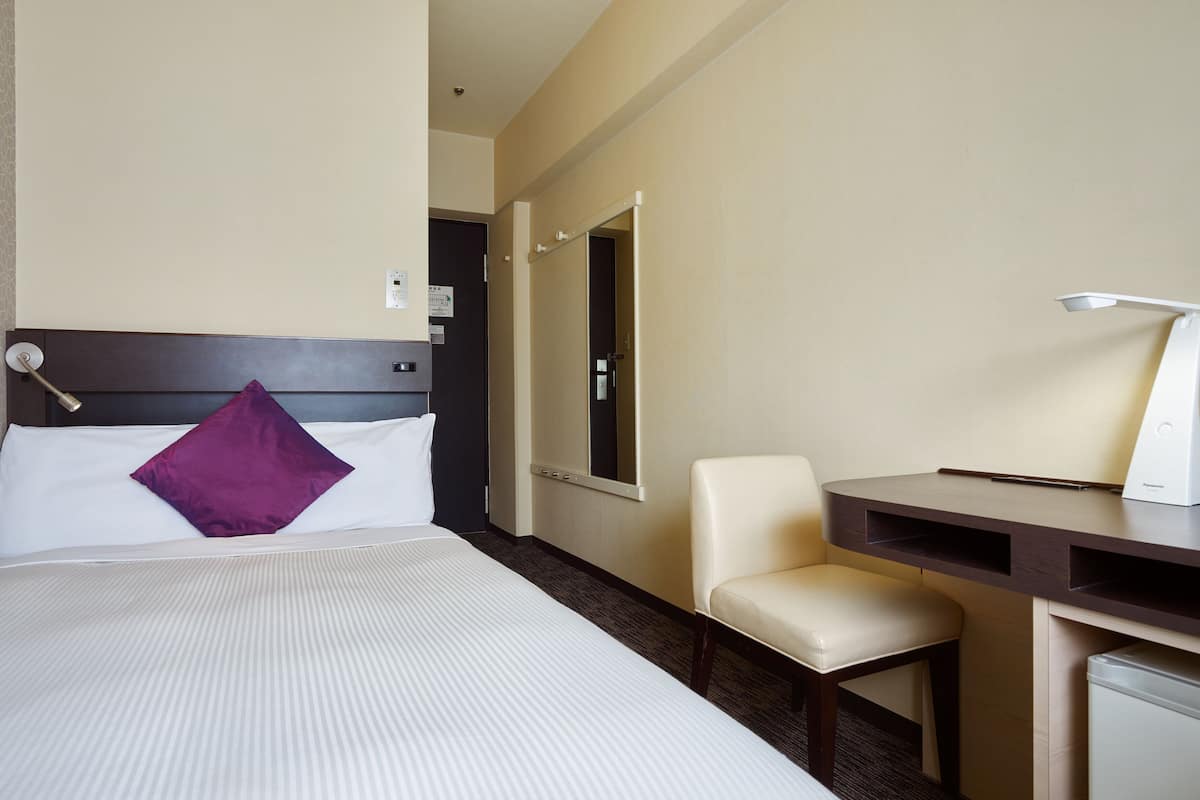 Una habitación de hotel con una cama, un escritorio, una silla y una lámpara de escritorio.