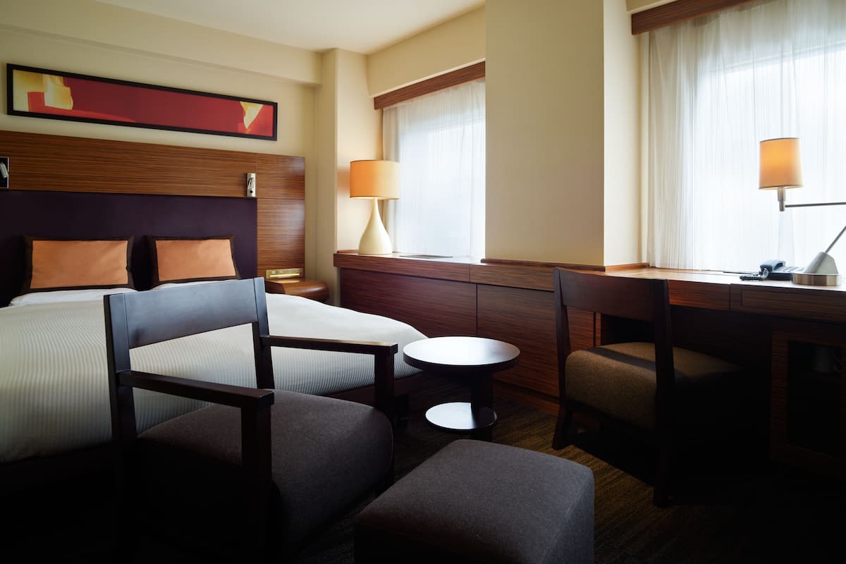 Una habitación de hotel con una cama, un escritorio, una silla, una mesita y una lámpara.