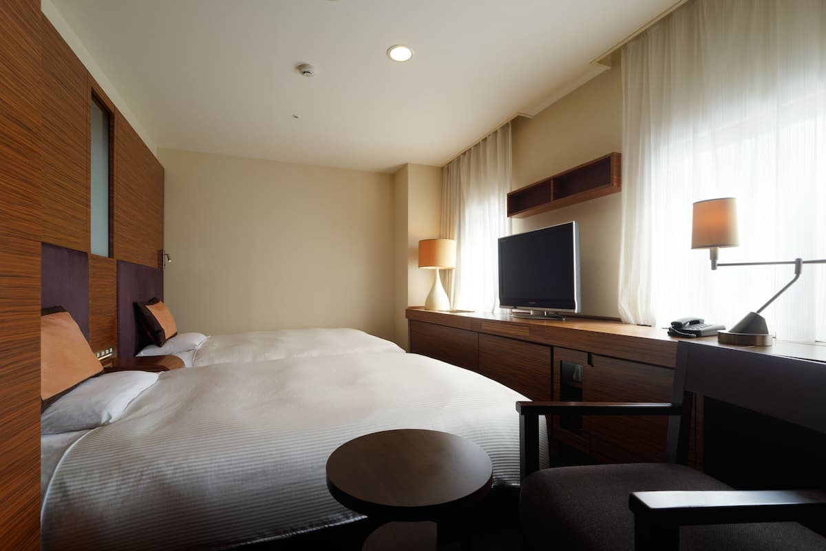 Habitación de hotel con una cama grande, un escritorio con televisor de pantalla plana, una silla, una mesita redonda y una lámpara.