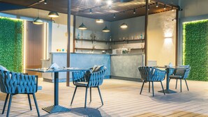 Een modern eetgedeelte buiten, met blauwe stoelen en een houten tafel, omgeven door een groene wand en afgedekt door een houten plafond.
