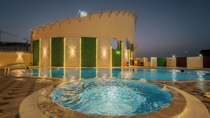Una piscina con un jacuzzi, una zona cubierta con techo curvo y una pared verde con luces verticales.