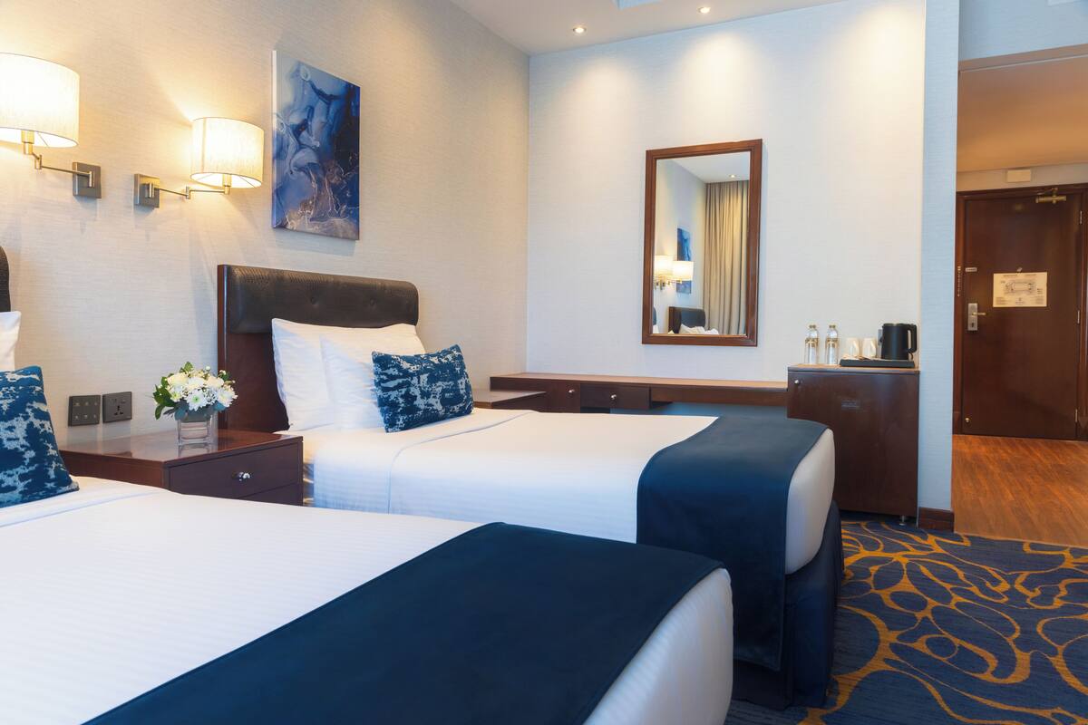 Habitación de hotel con dos camas, un escritorio, un espejo y lámparas de pared.