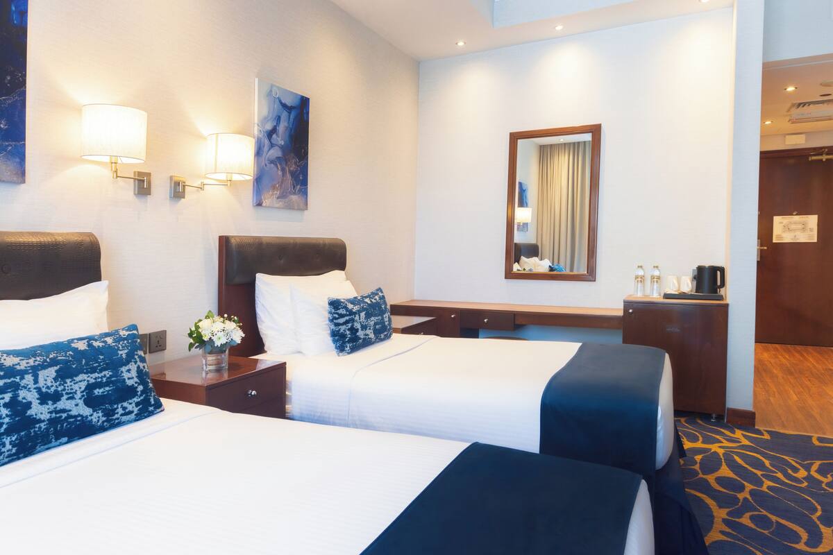 Habitación de hotel con dos camas, un escritorio, un espejo y lámparas de pared.
