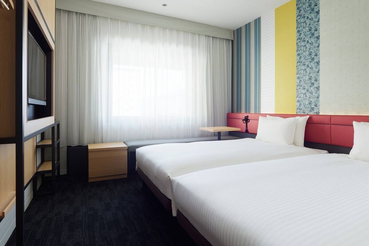 Ein Hotelzimmer mit einem großen Bett, einem Schreibtisch, einem Kleiderschrank und einem Fenster mit Vorhängen.