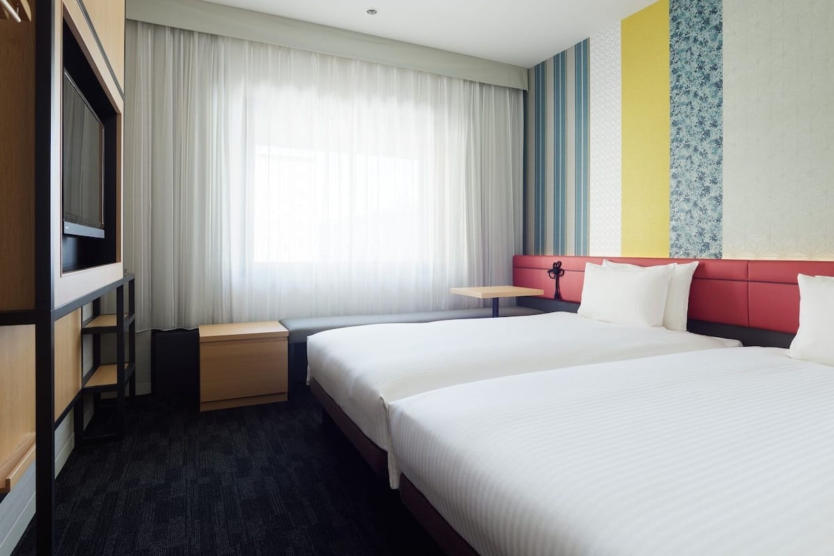Hotellihuone, jossa on suuri sänky, työpöytä, vaatekaappi ja ikkuna, jossa on verhot.