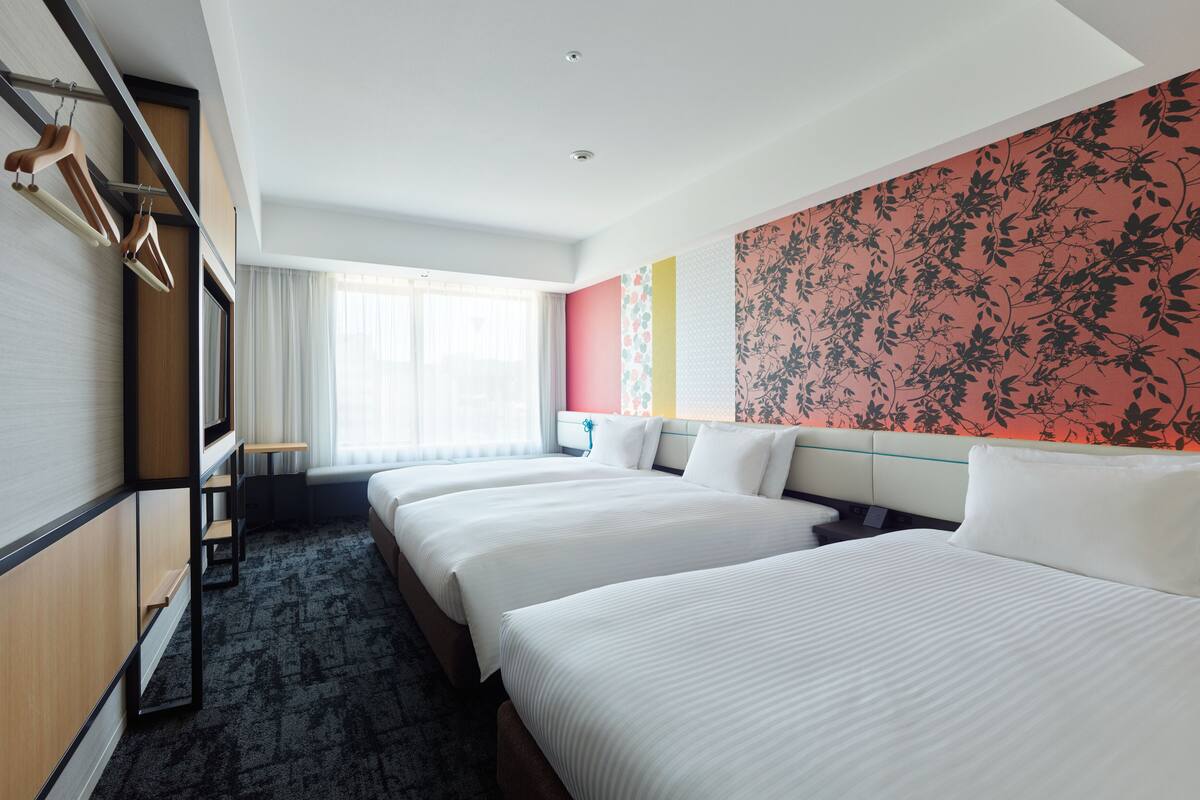 Ein Hotelzimmer mit zwei Betten, einem Schreibtisch und einem Fenster mit Vorhängen.