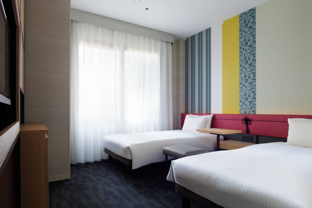Ein Hotelzimmer mit zwei Betten, einem Schreibtisch und einem Fernseher.