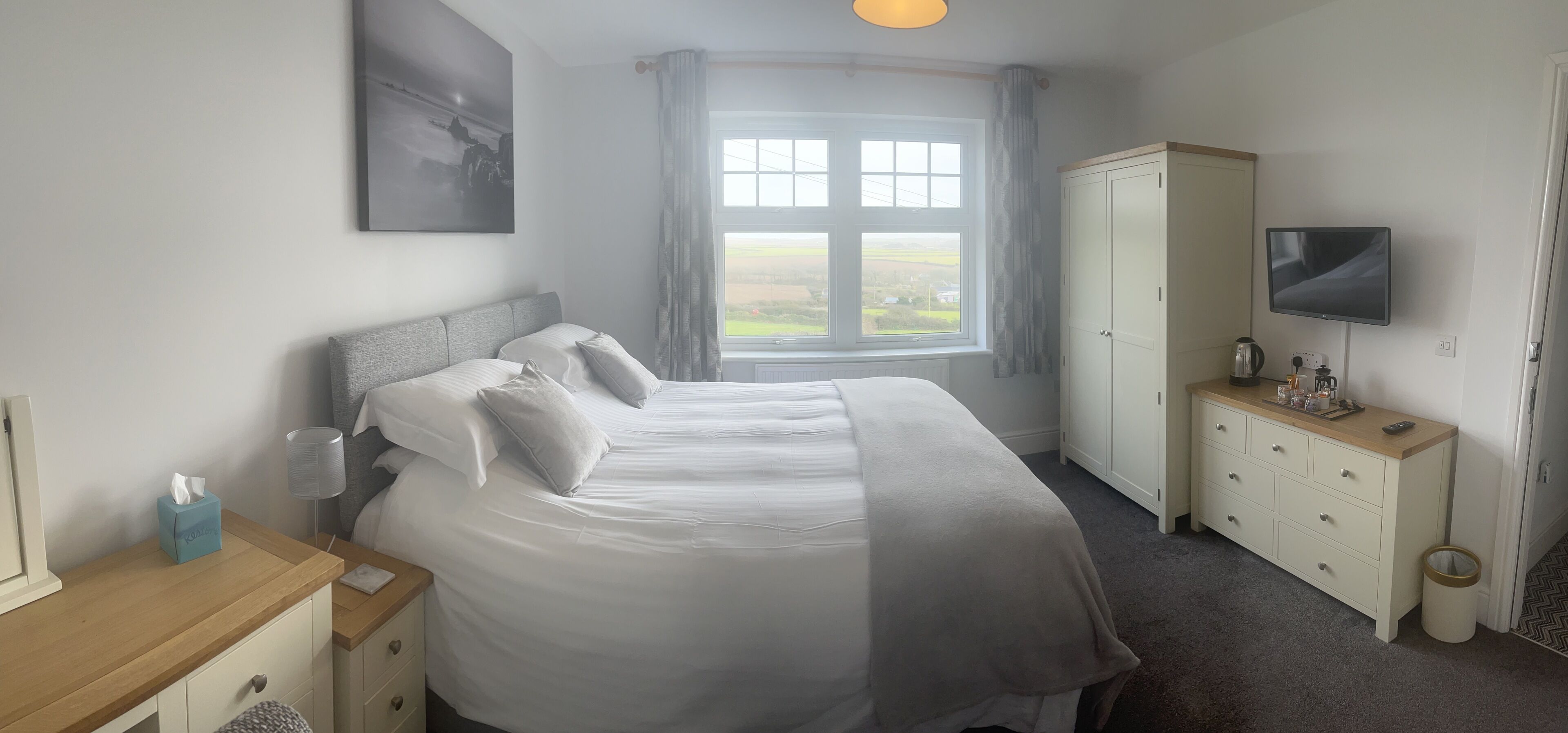 A neatly arranged bedroom with a large bed, a bedside table with a lamp, a wardrobe, and a TV mounted on the wall.