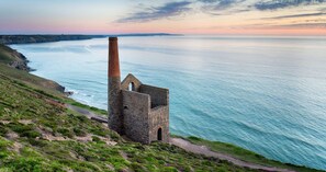 A coastal lighthouse structure with a tall chimney, situated on a grassy cliff overlooking the sea.