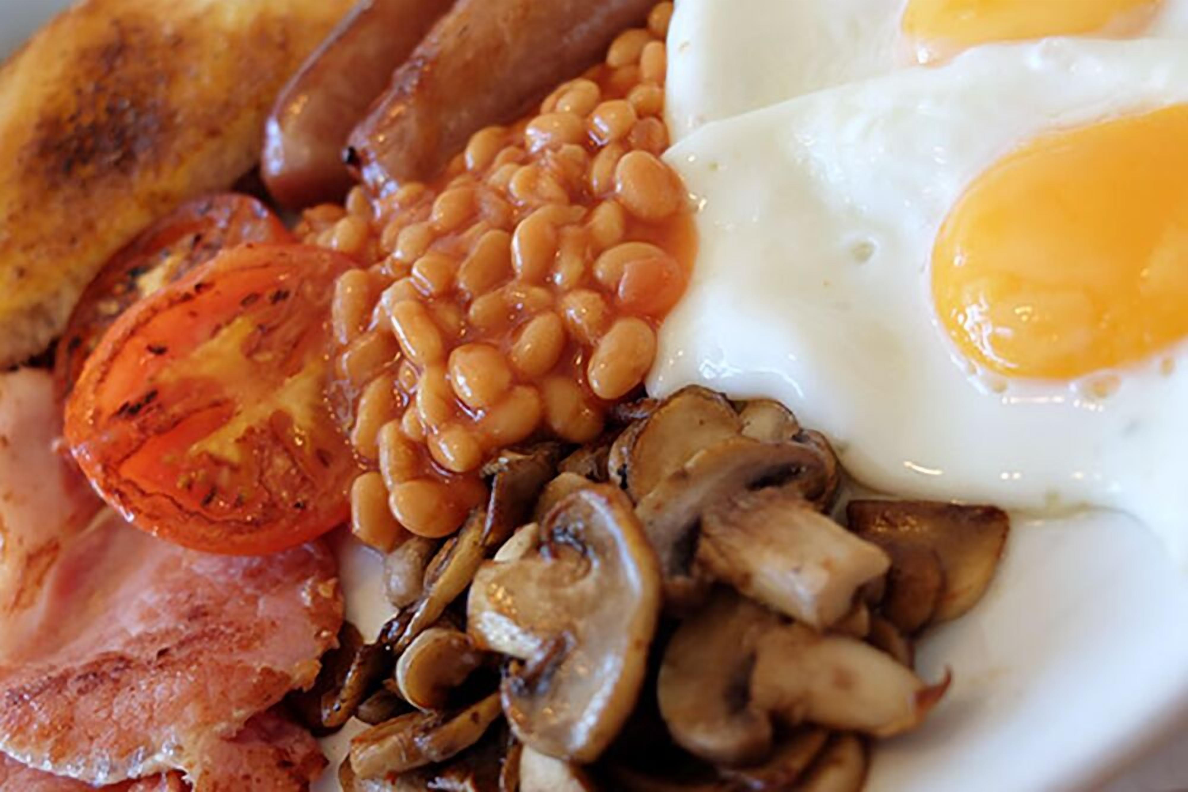 A breakfast plate with eggs, sausages, beans, mushrooms, tomatoes, and bacon.