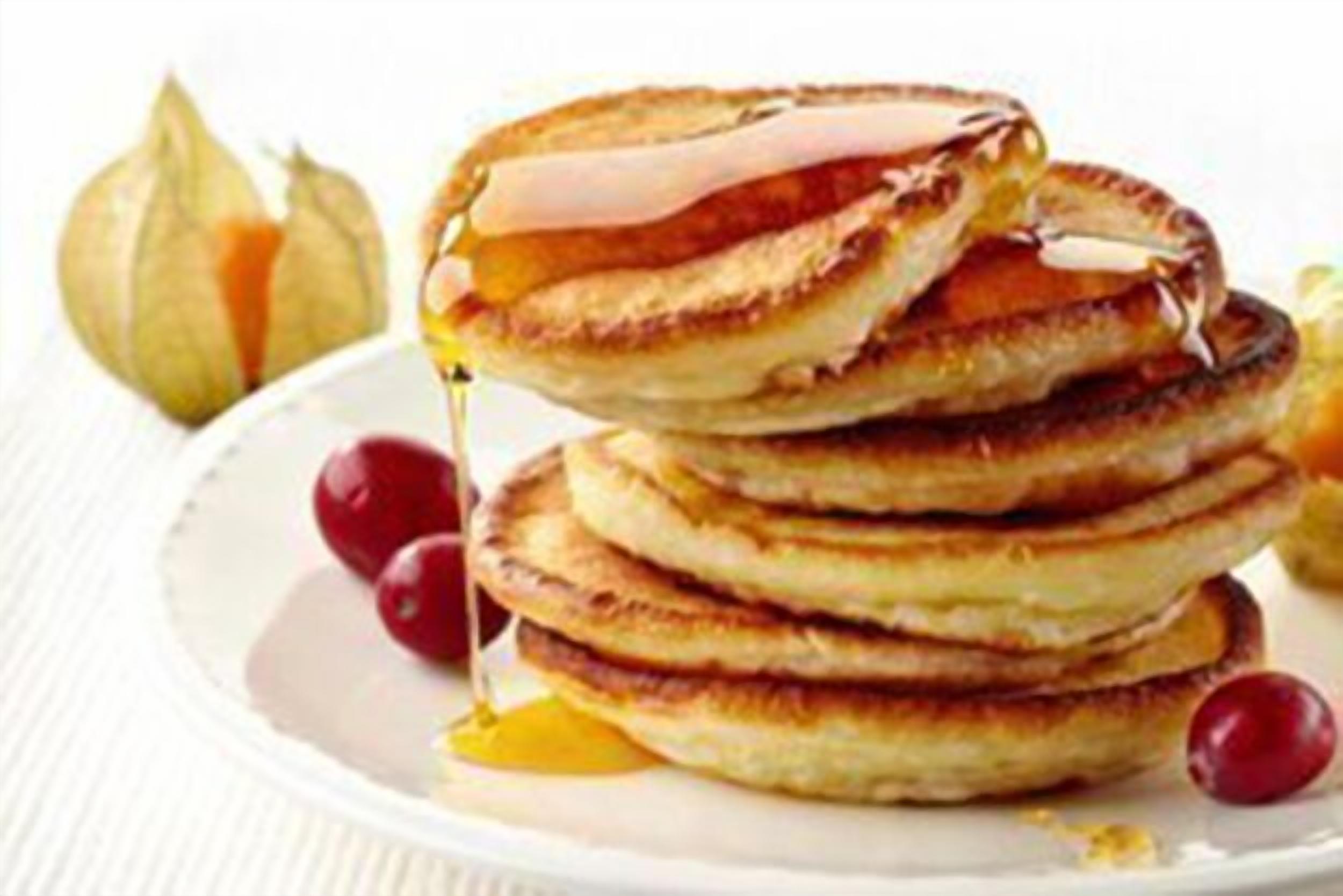 Une pile de crêpes arrosées de sirop et garnies de cerises.