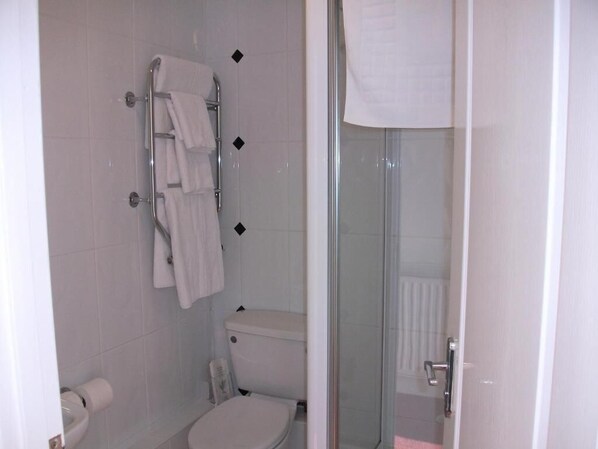 A bathroom with a toilet, a glass shower enclosure, and a towel rack with multiple towels.